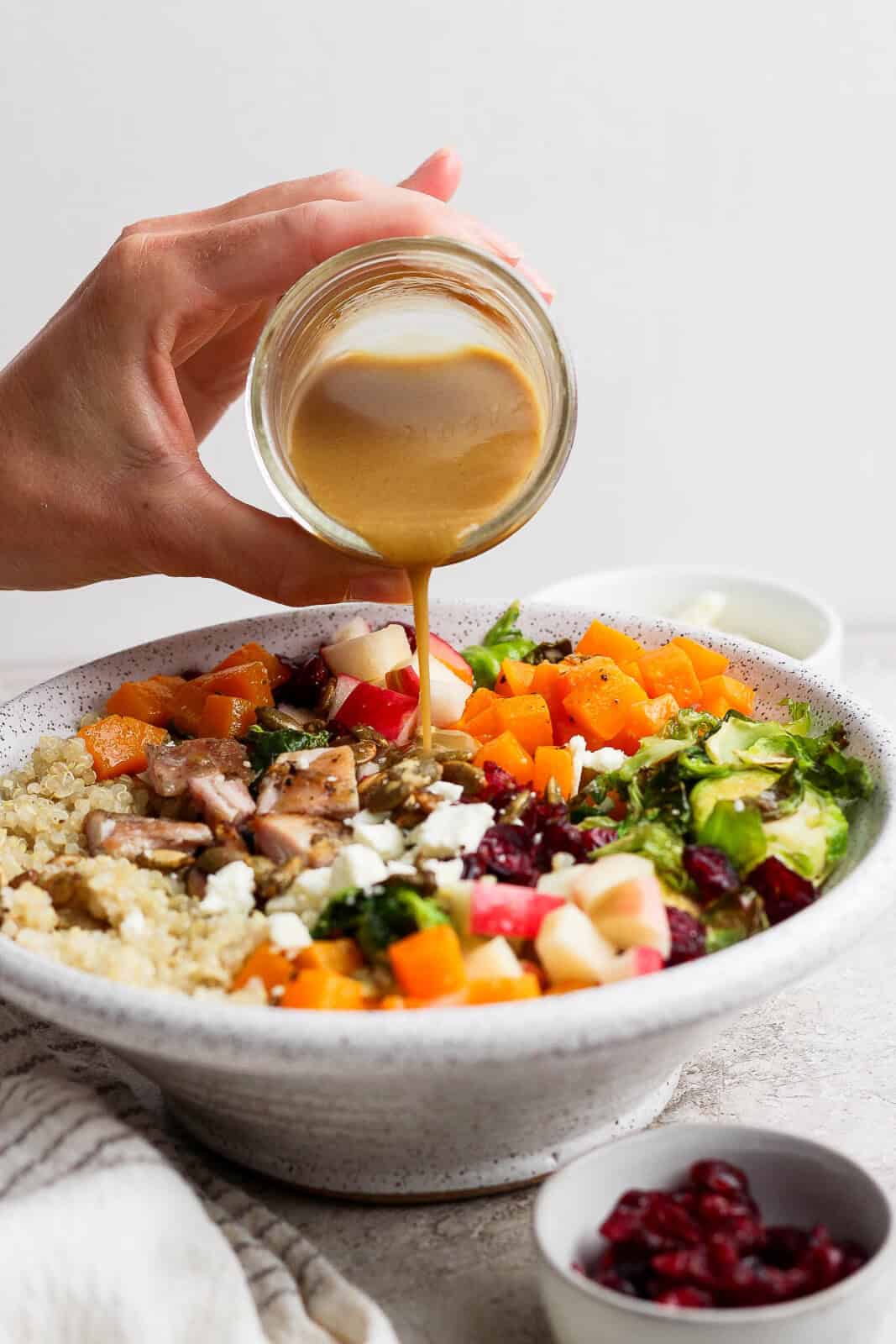 Maple dijon dressing being poured on an Autumn harvest bowl.