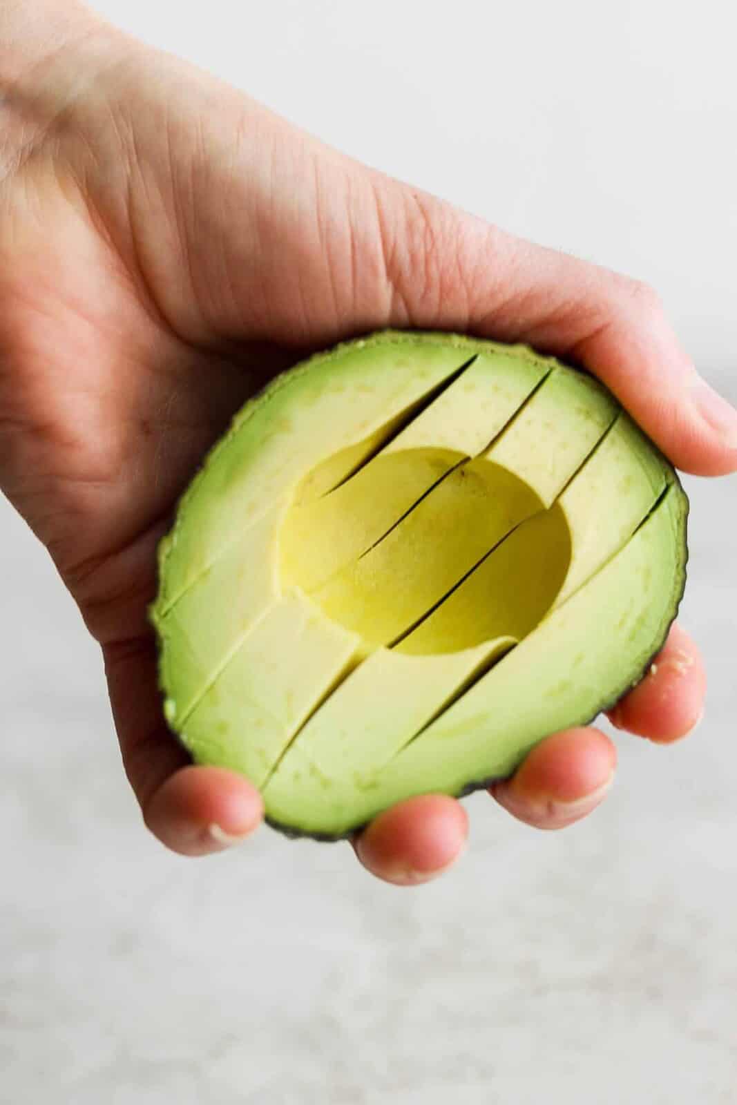 A hand holding a sliced avocado for an avocado egg bowl.