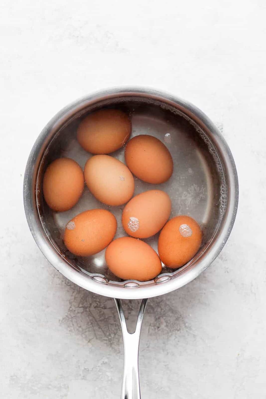 Soft boiled eggs cooking in a pot of water for an avocado egg bowl.