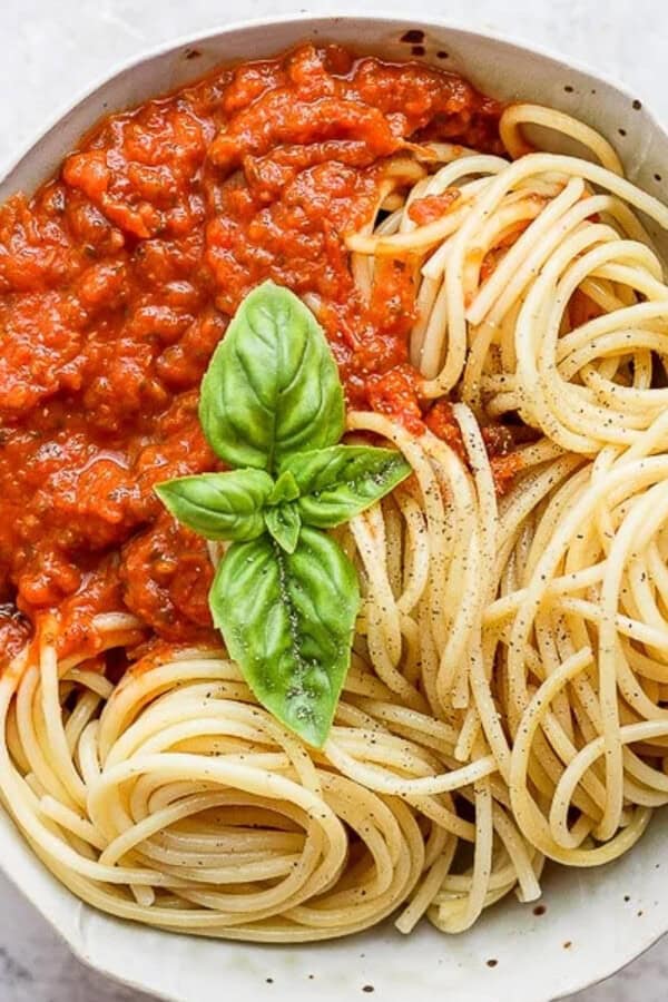 A bowl of the best homemade marinara sauce with noodles and fresh basil.