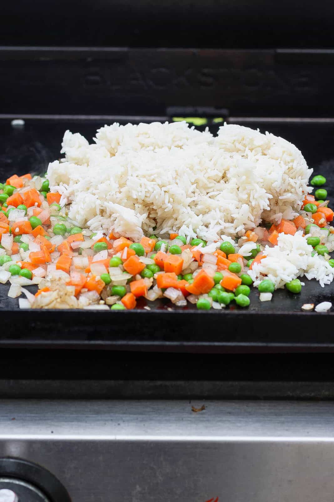 Rice added to the veggies on the griddle for Blackstone shrimp fried rice.