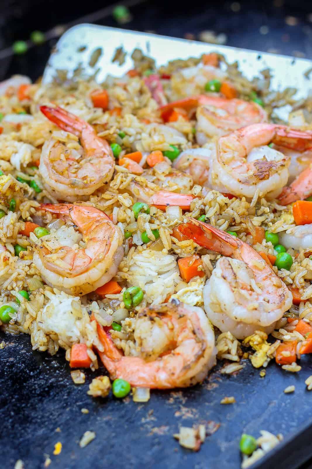 A metal spatula tossing Blackstone shrimp fried rice together on the griddle.