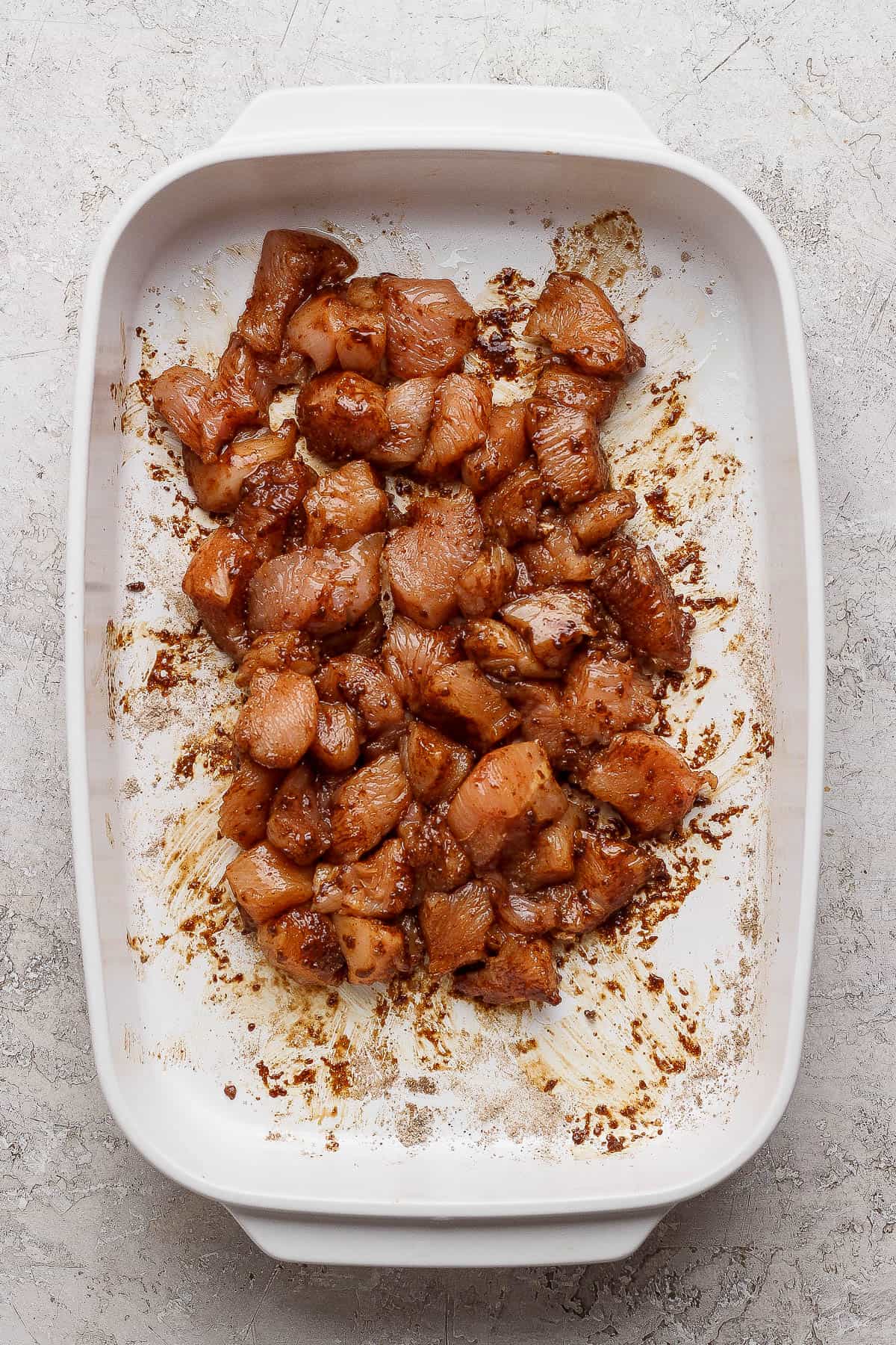 Seasoned and cubbed chicken breasts in a casserole dish to make Chicken fajita casserole with rice.