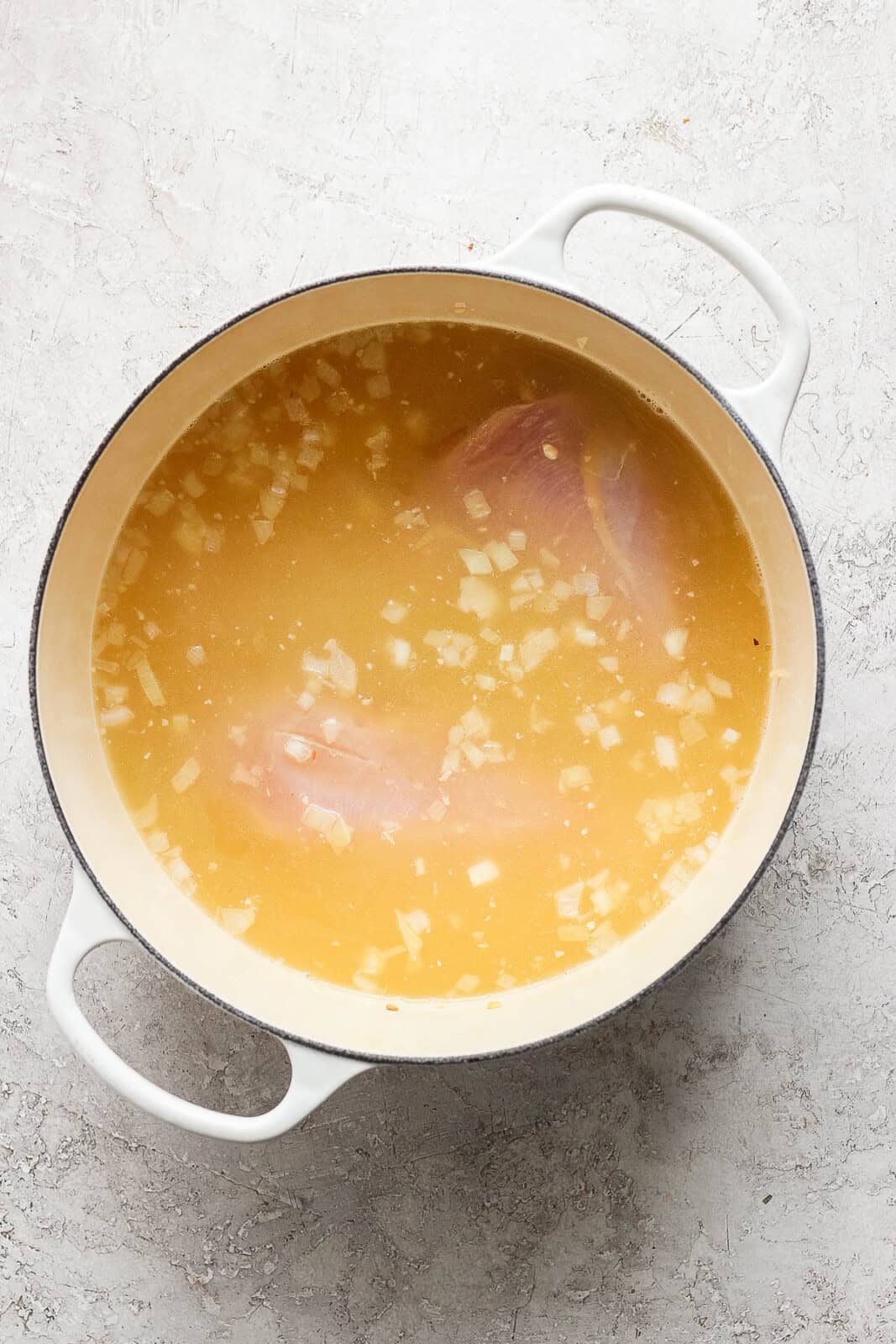 Broth and raw chicken breasts added to onion and garlic in a pot for chicken taco soup.