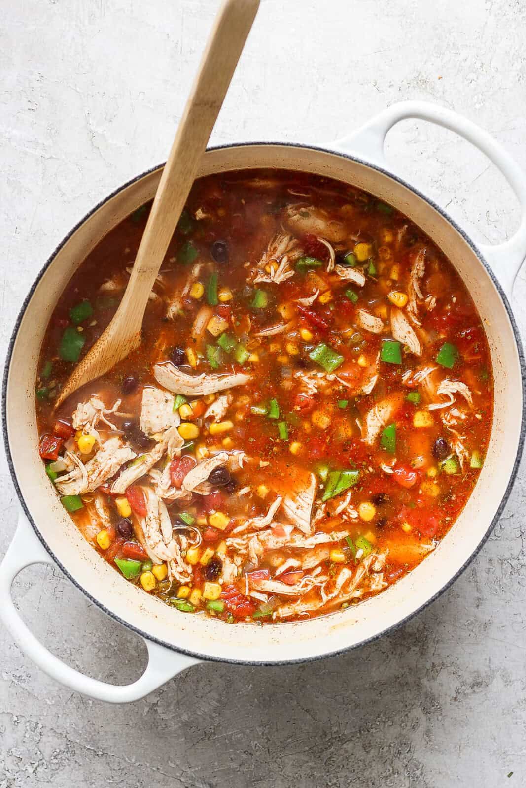 Mixed chicken taco soup in a pot with a wooden spoon before the cream cheese is added.