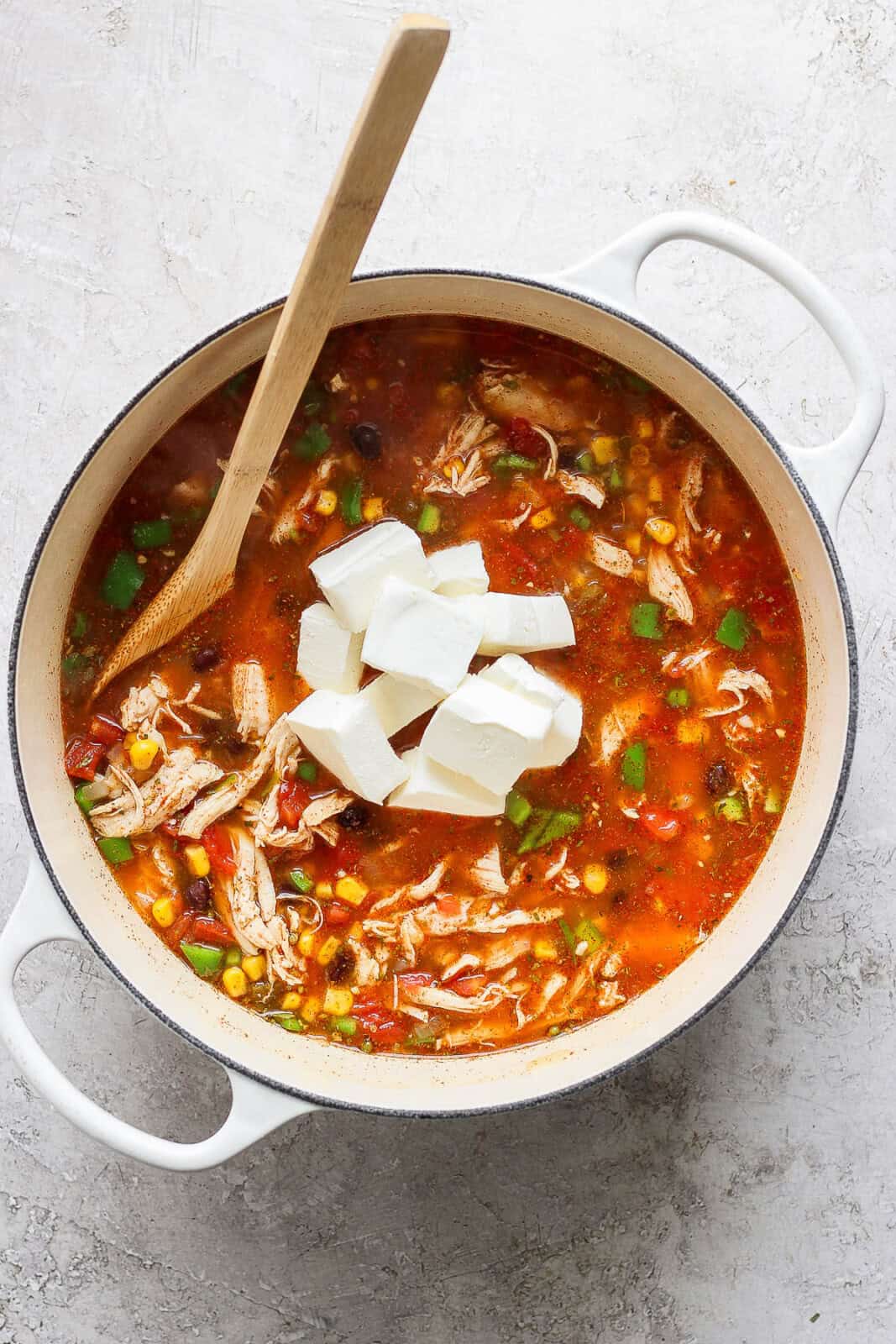 Chunks of cream cheese added to a pot of chicken taco soup.