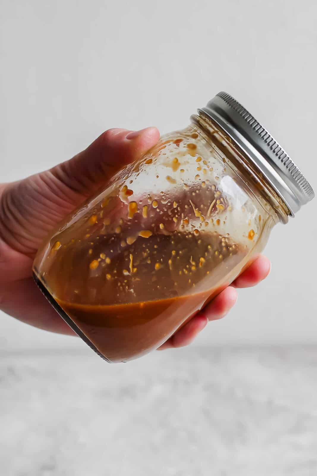 A hand holding a jar of chow mein sauce.