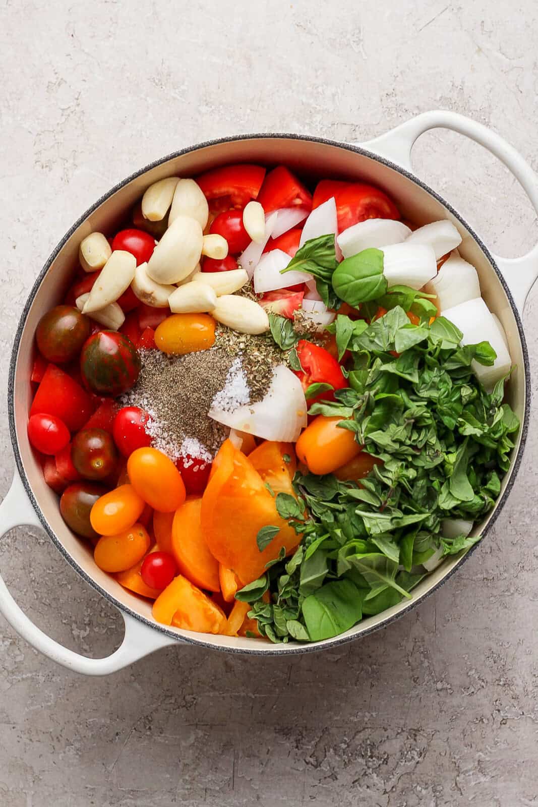 All of the ingredients for homemade marinara sauce separated in a white dutch oven.