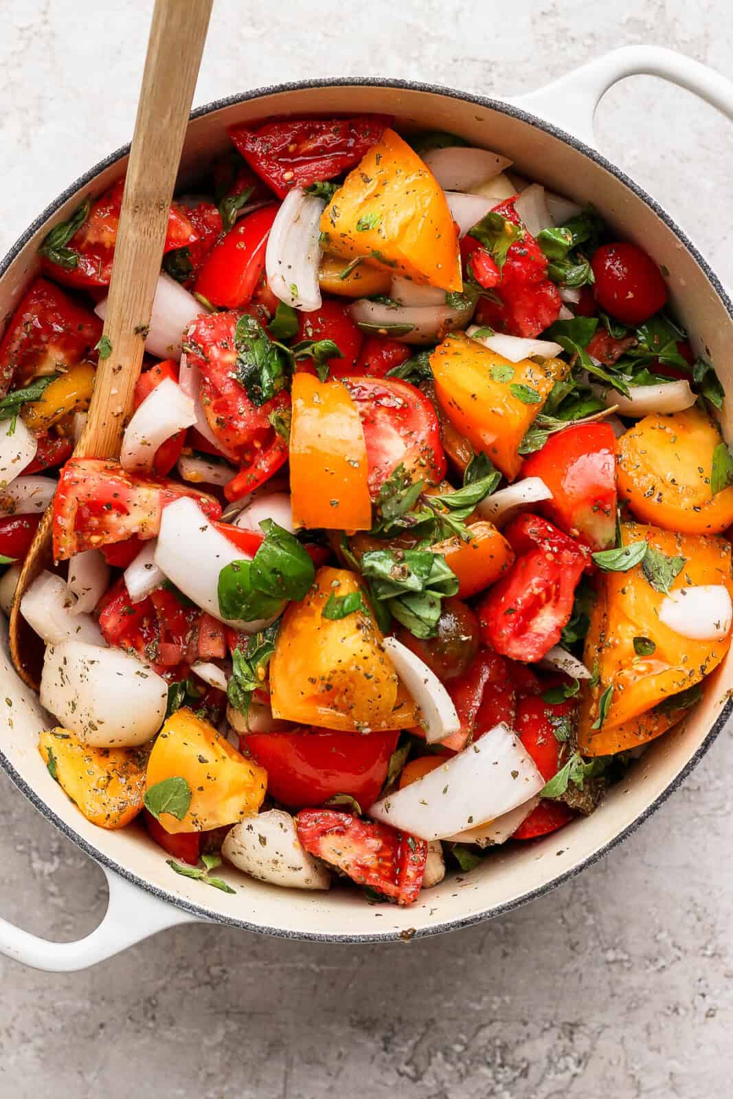 All of the ingredients for homemade marinara sauce mixed together in a white dutch oven with a wooden spoon.