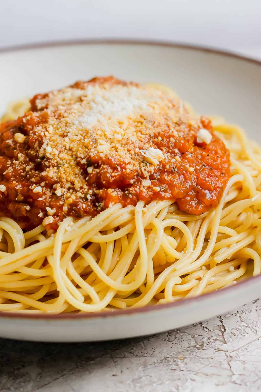 The best homemade marinara sauce on top of spaghetti noodles with grated parmesan cheese in a bowl.