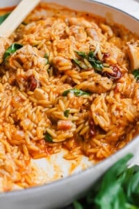 Marry me chicken orzo in a white braising pan with a wooden spoon sticking out the side.