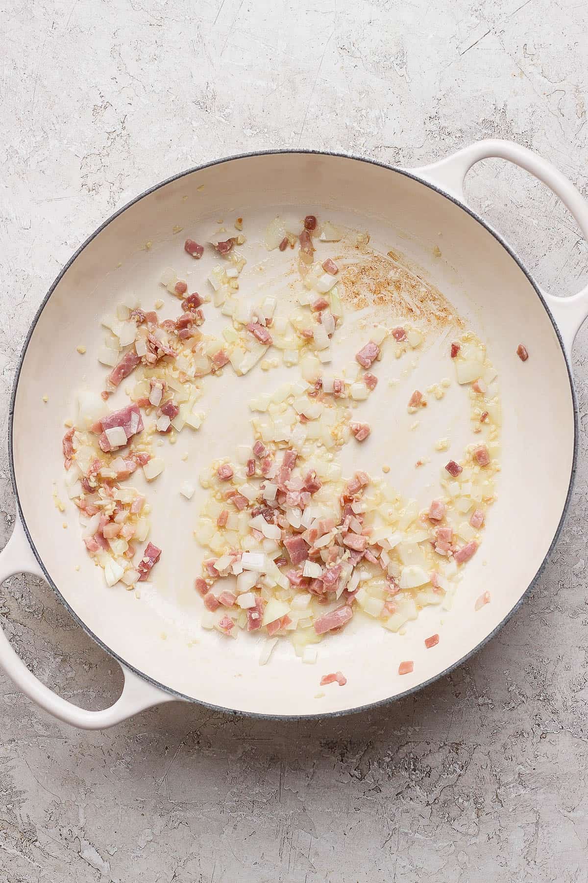 Oil, garlic, onion, and pancetta in a skillet to make marry me chicken orzo.