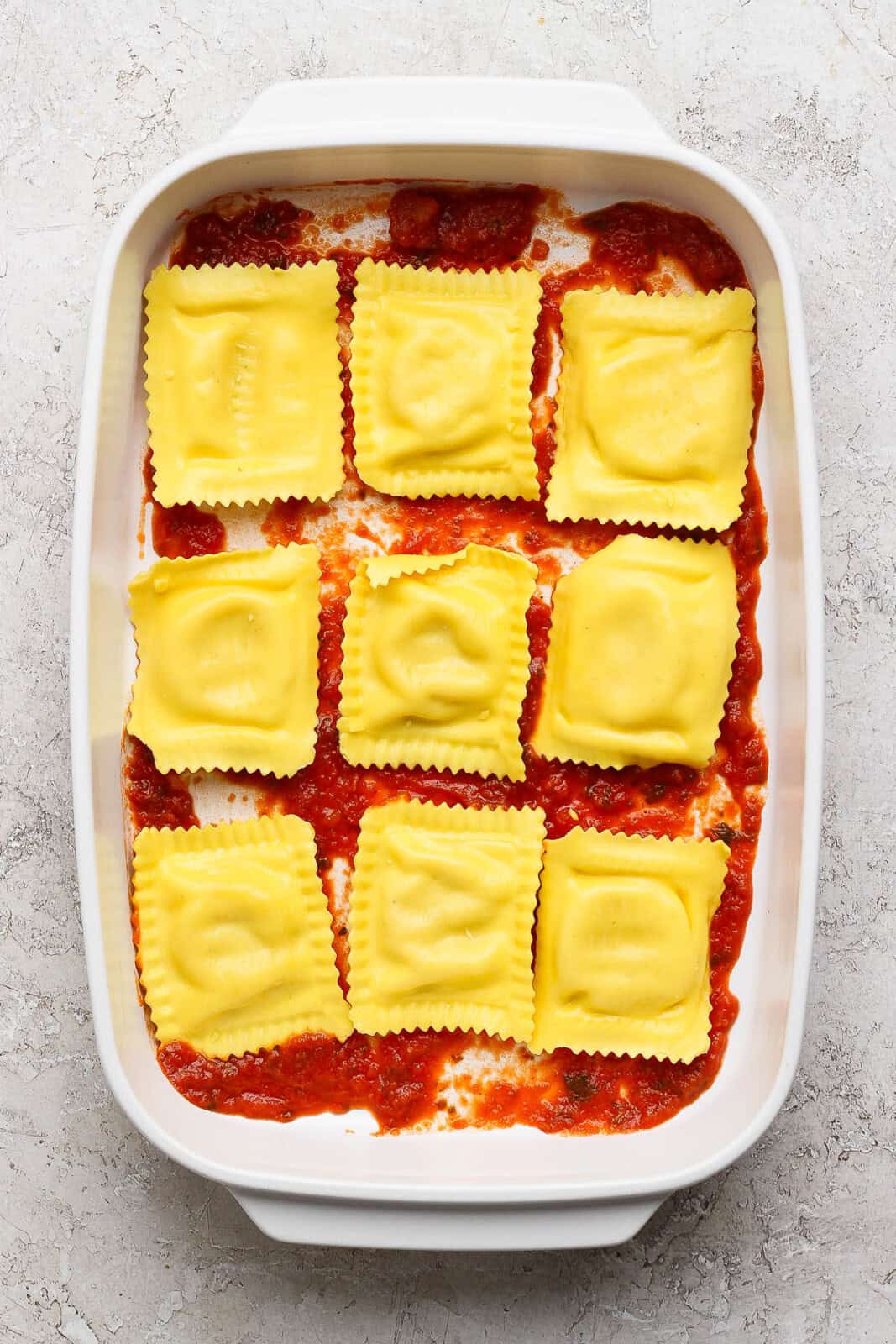 A little marinara sauce and nine ravioli on the bottom of a baking dish for million dollar ravioli casserole.