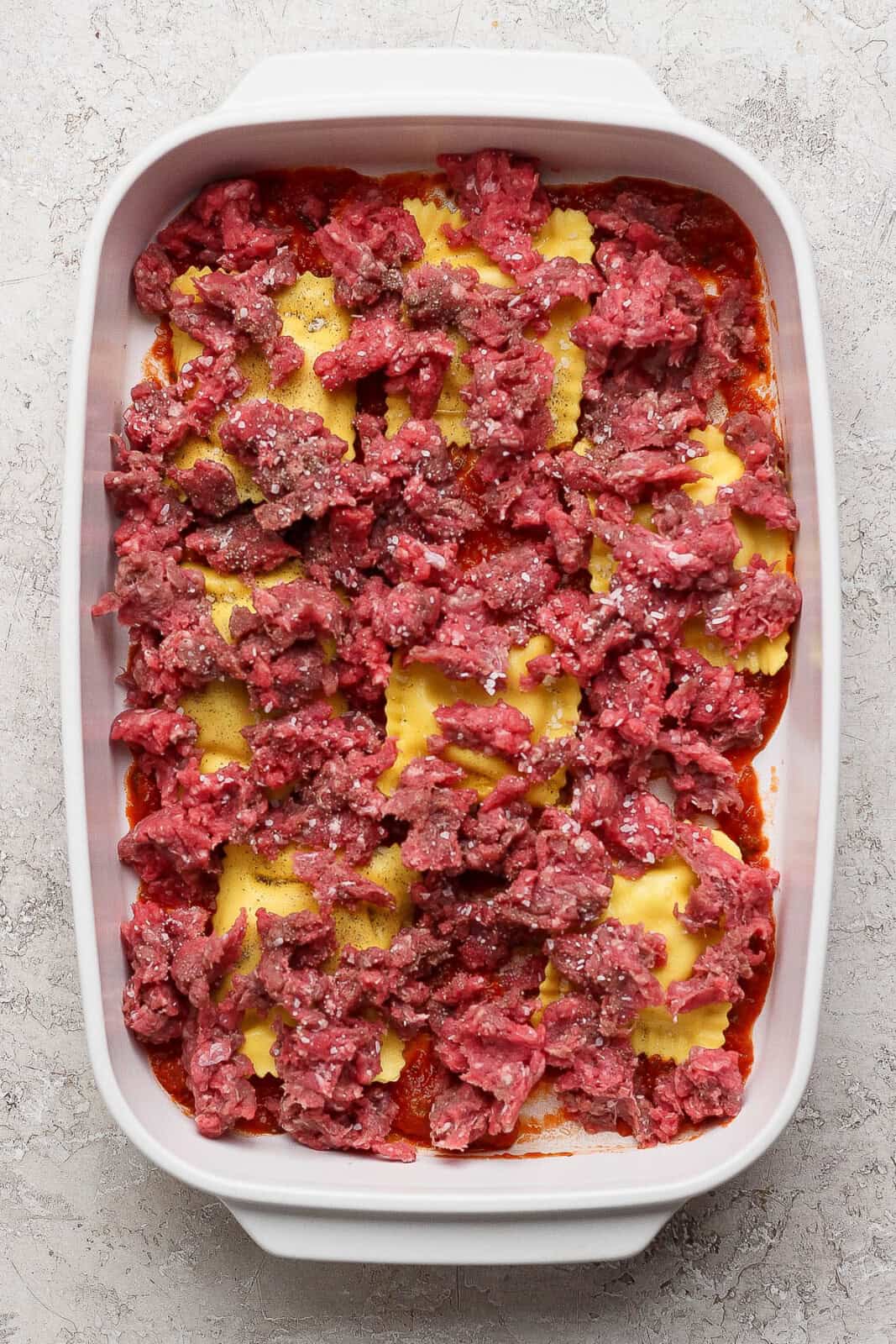 Crumbled, raw ground beef on top of ravioli to make million dollar ravioli casserole.