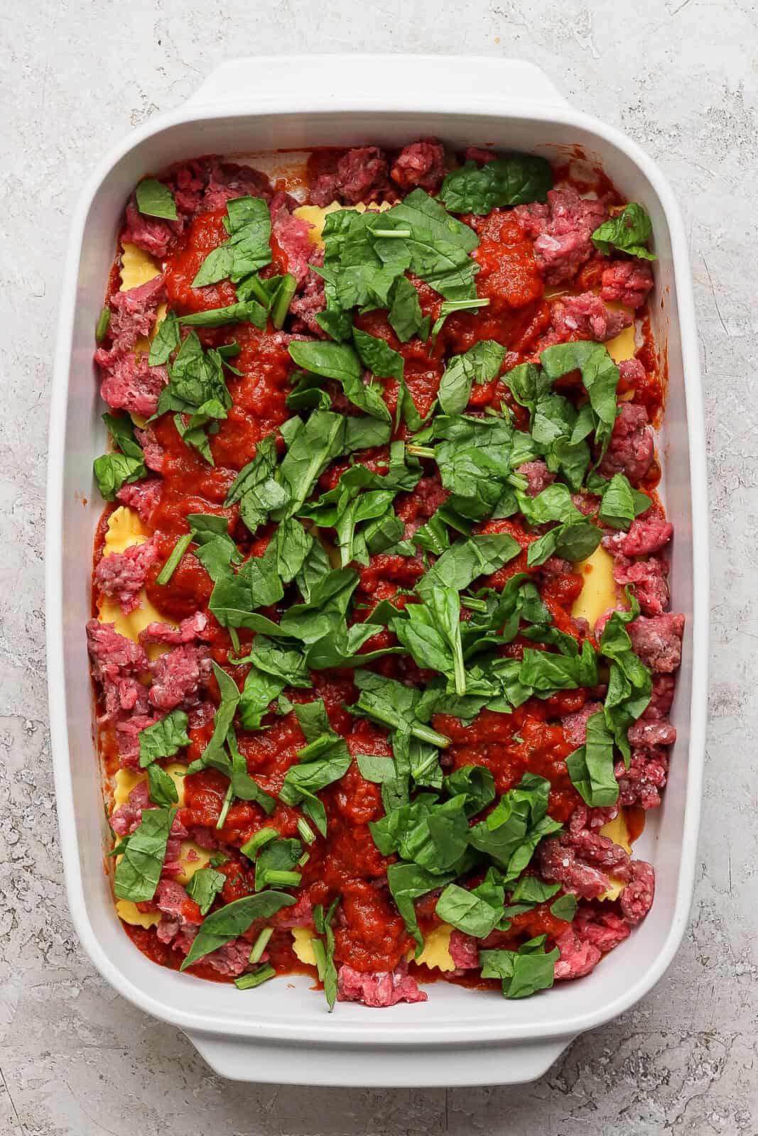 More sauce and fresh spinach added to the middle of a million dollar ravioli casserole.
