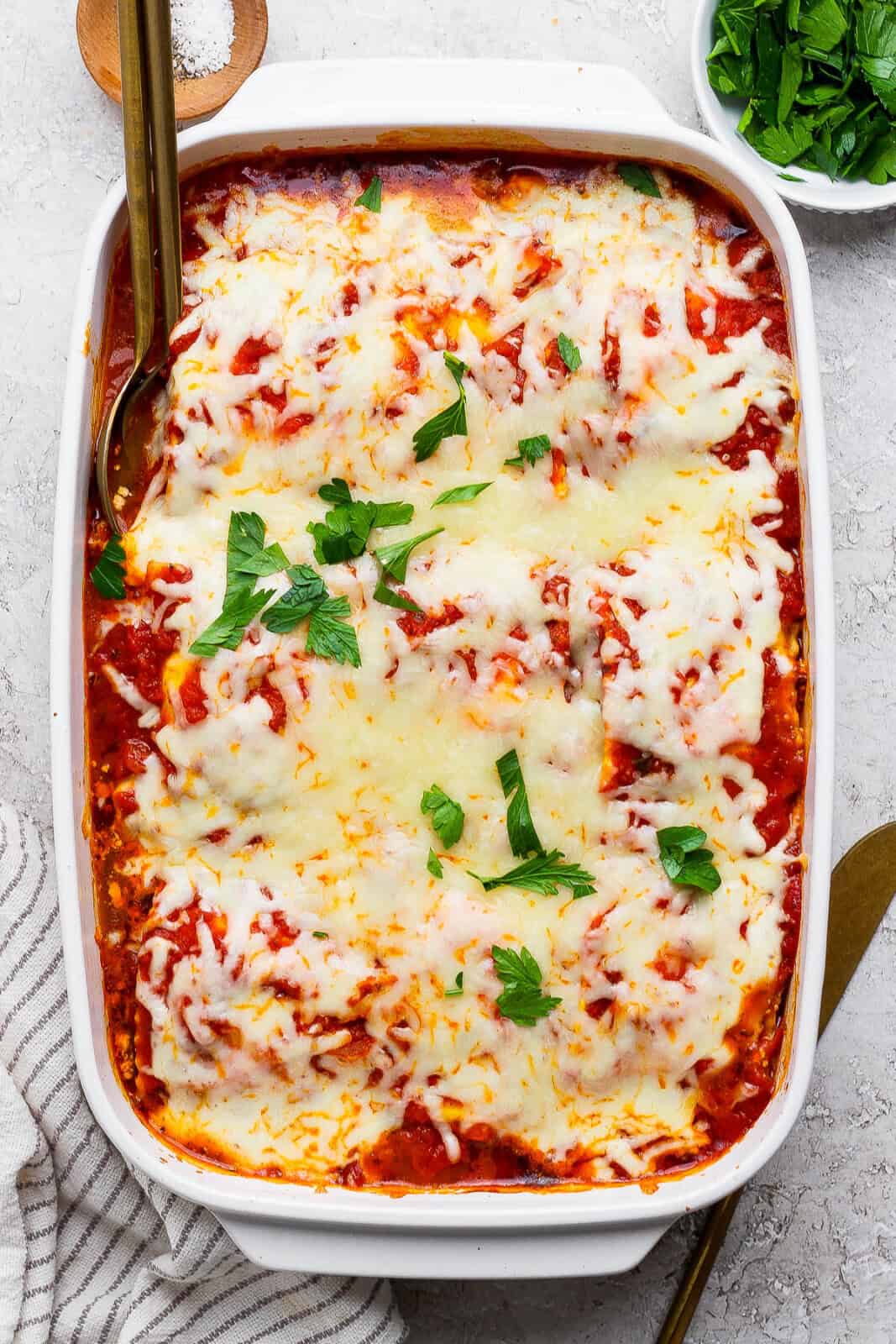 A fully baked million dollar ravioli casserole with cheese on top and two gold spoon sticking out the side.