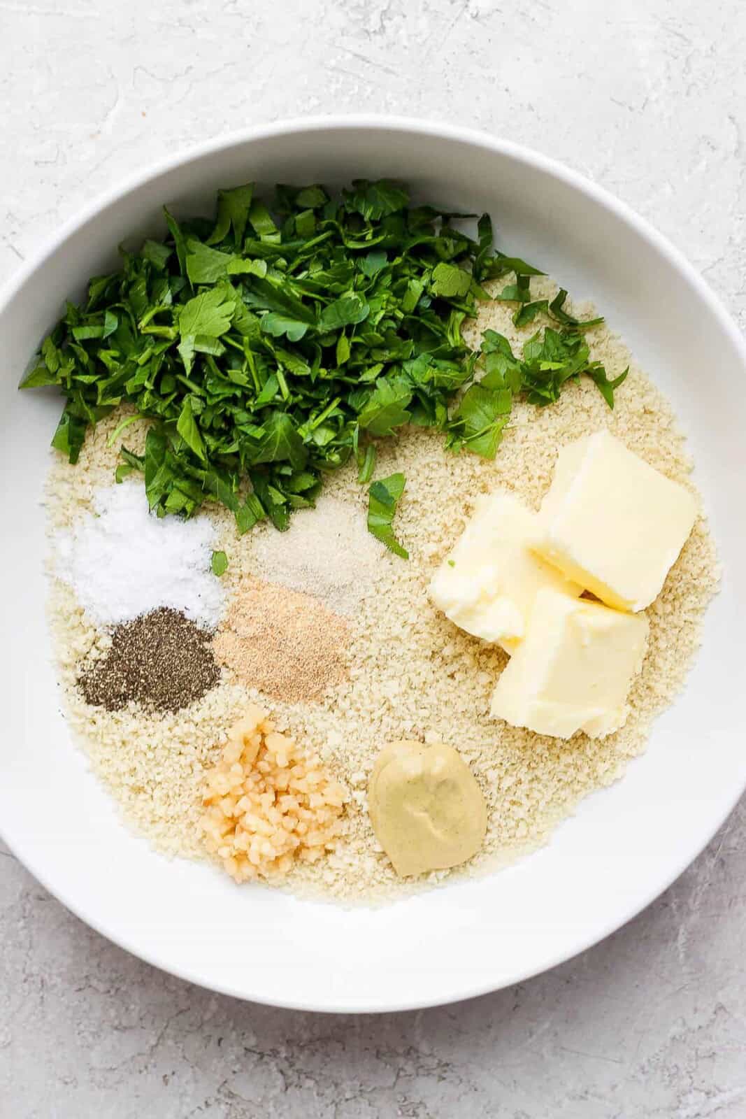 Panko breadcrumbs, butter, garlic, dijon mustard, fresh parsley and seasonings in a white bowl for making panko crusted salmon.