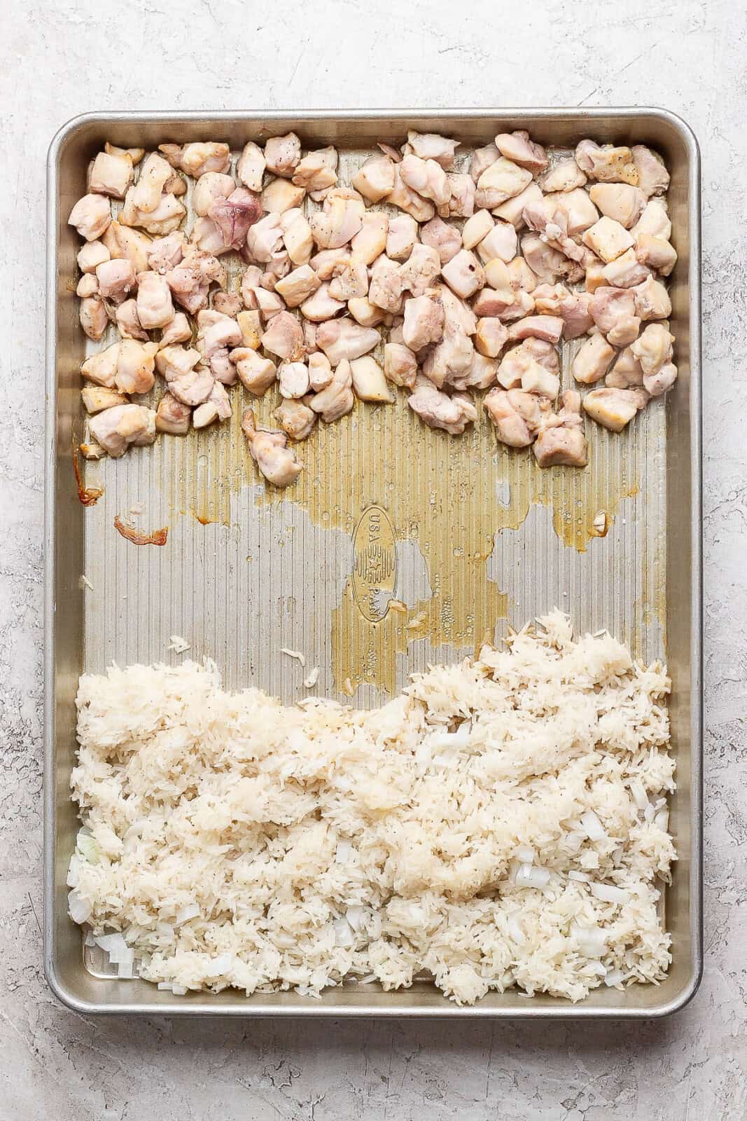 A sheet pan with cooked chicken on one side and rice with onions on the other side to make sheet pan fried rice.
