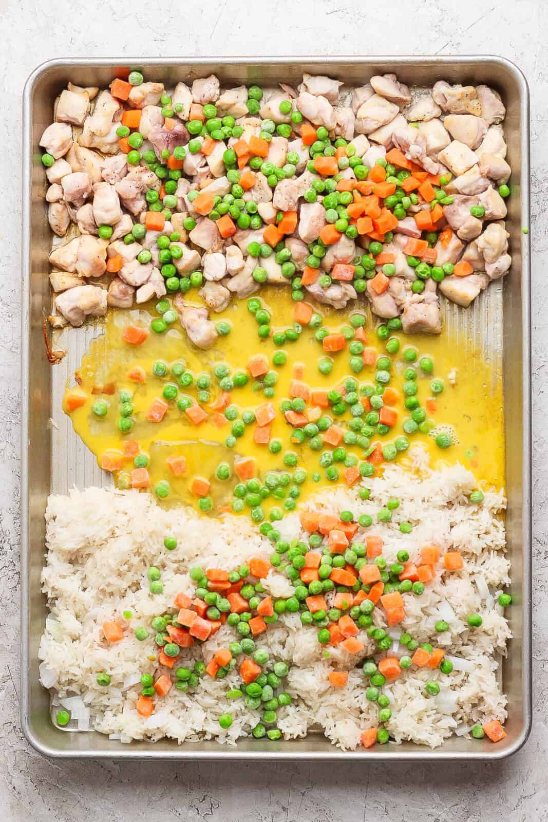 Frozen peas and carrots and whisked eggs added to the sheet pan fried rice before baking.