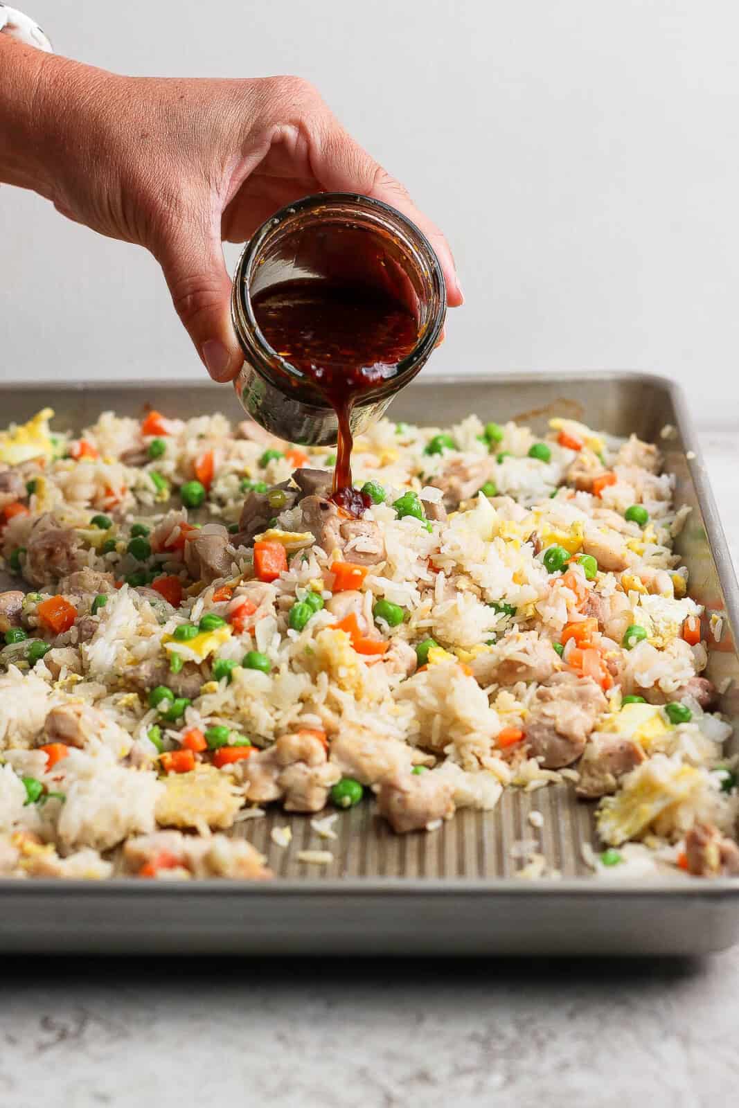 Fried rice sauce being poured over the fully cooked sheet pan fried rice.