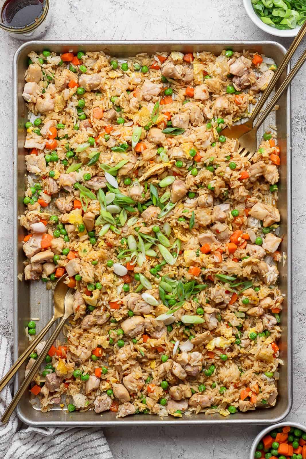 Sheet pan fried rice fully cooked with green onions on top and gold silverware sticking out the sides.