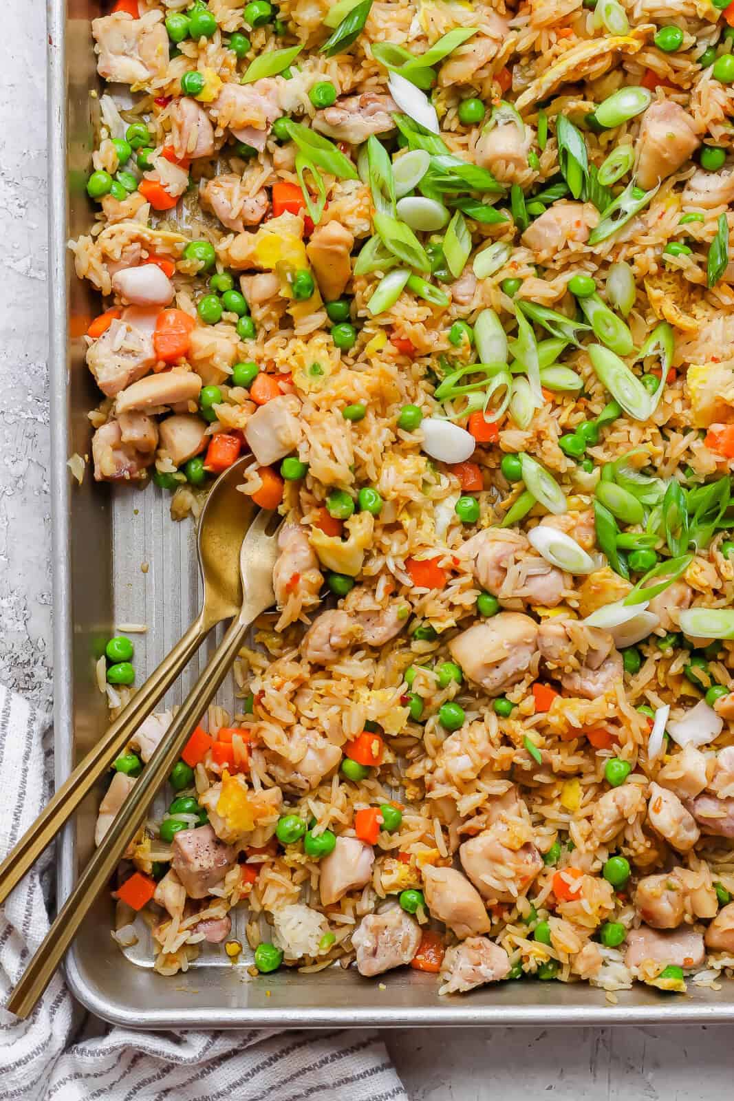 Sheet pan fried rice with a gold fork and spoon sticking out the side.
