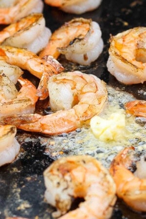 Several shrimp on the blackstone cooking with garlic butter.