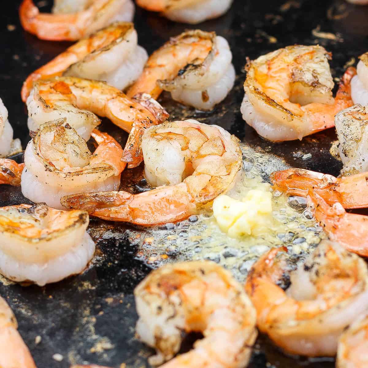 Several shrimp on the blackstone cooking with garlic butter.