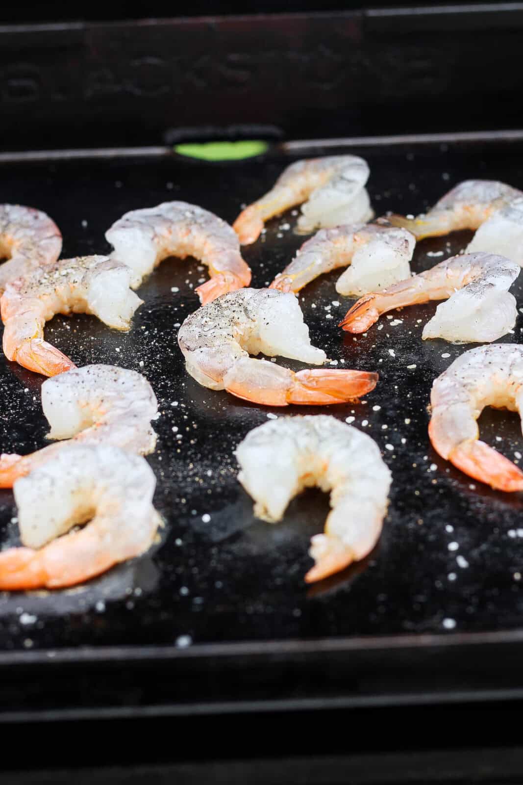 Raw shrimp in a single layer on the Blackstone with salt and pepper.