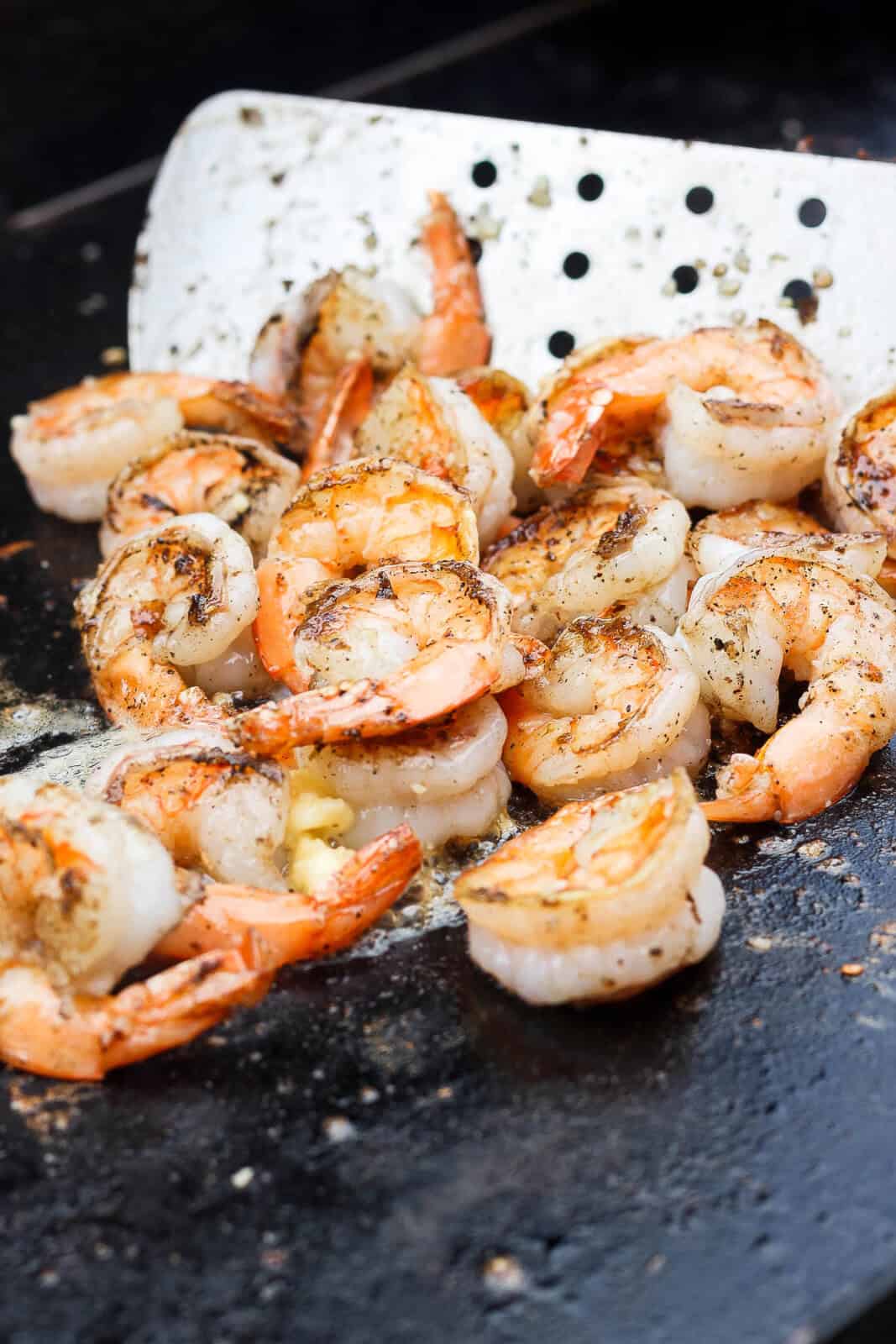 A large spatula tossing shrimp on the blackstone in garlic butter.