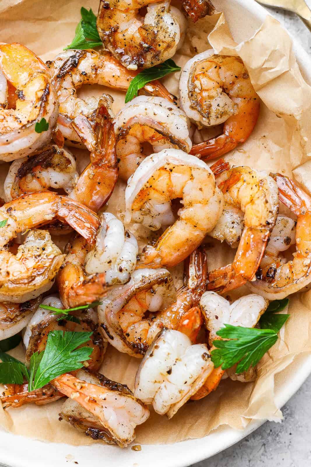 Several garlic butter shrimp in a bowl with parchment paper.