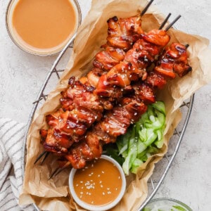Thai chicken skewers in a basket with a peanut dip and marinated cucumbers.