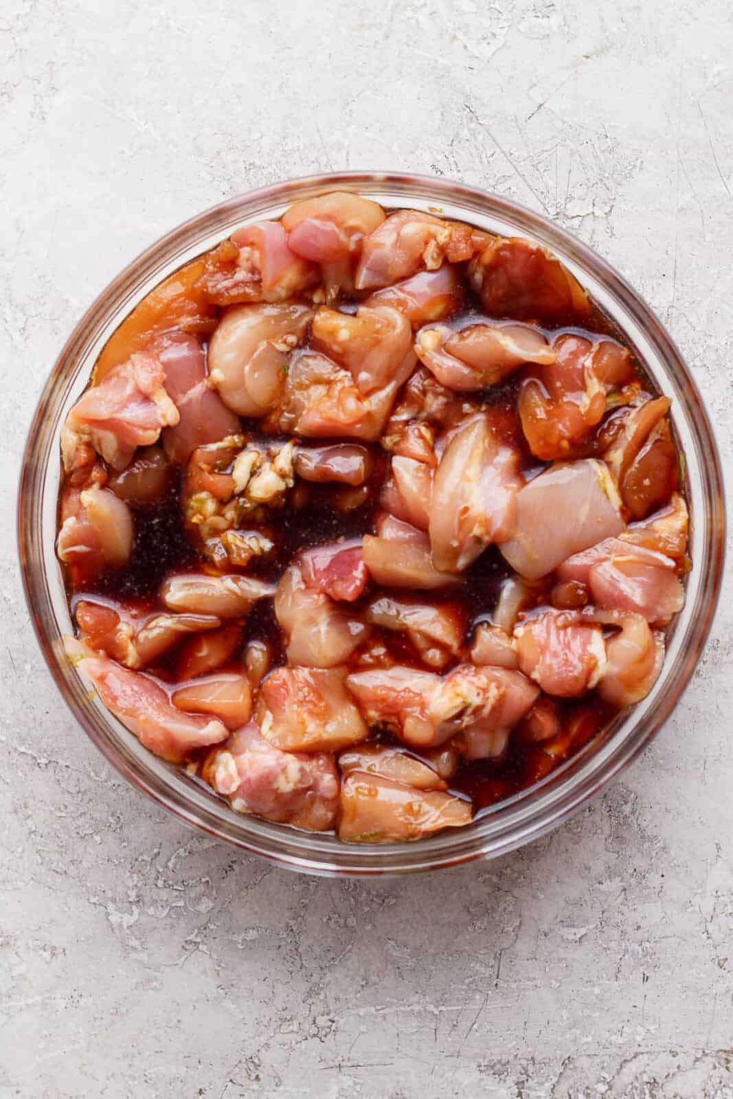 Chicken thigh pieces marinating in a bowl before making Thai chicken skewers.