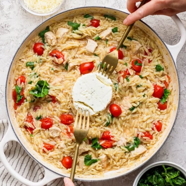 Boursin orzo with chicken in a large braiser with the Boursin cheese in the middle being pulled apart with two forks.