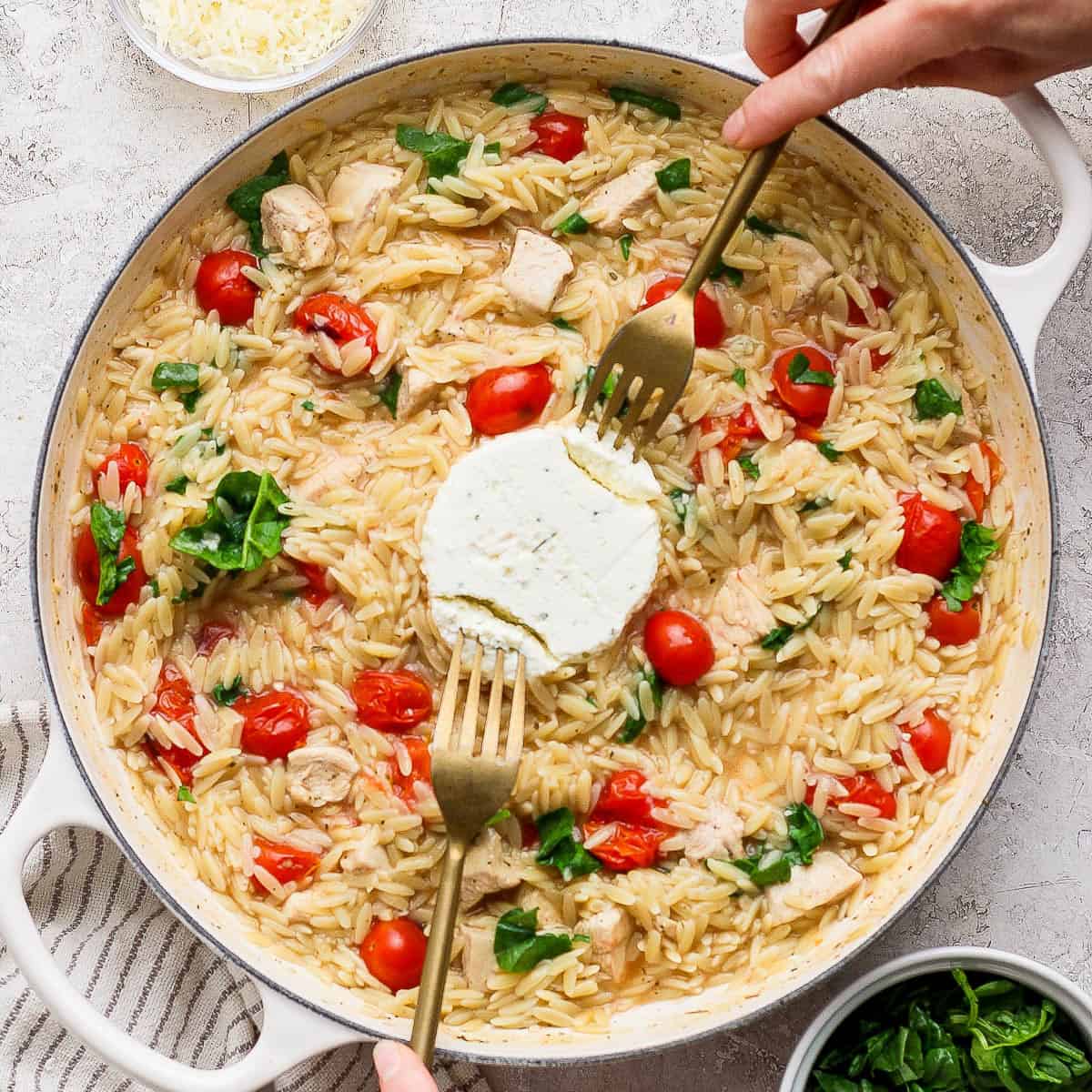 Boursin orzo with chicken in a large braiser with the Boursin cheese in the middle being pulled apart with two forks.