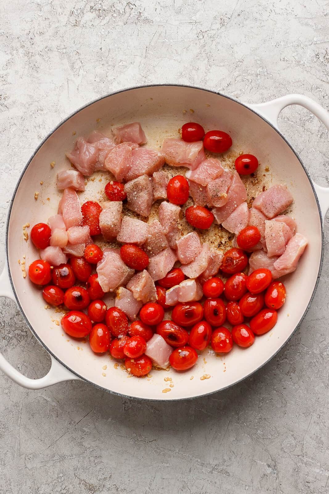 Pieces of raw chicken added to the blistering tomatoes in a braiser to make boursin orzo.