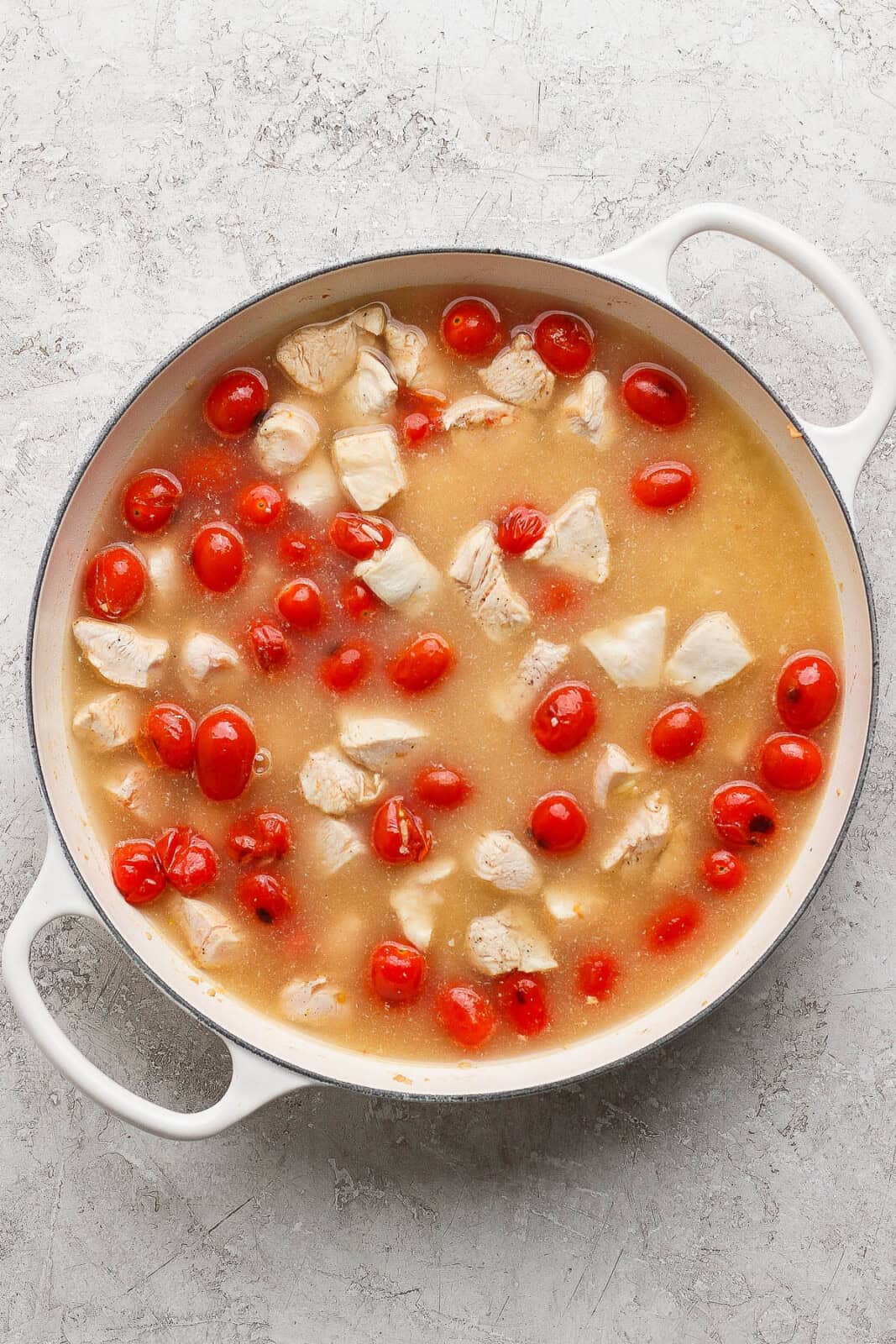 Orzo, chicken, and tomatoes simmering in chicken broth to make boursin orzo.