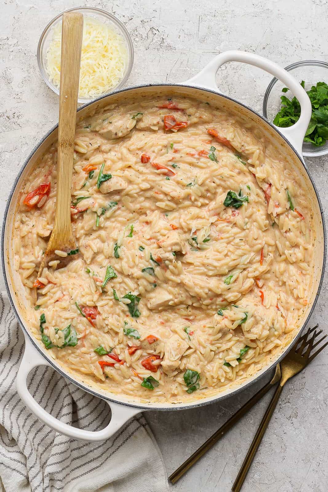 Boursin orzo with chicken fully cooked in a braising pan with a wooden spoon sticking out the side.