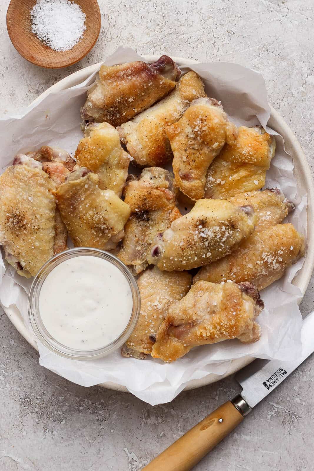 Oven baked chicken wings in a parchment-lined bowl with a dish of ranch dressing.