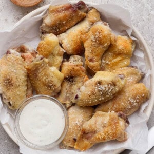 Baked chicken wings in a bowl lined with parchment paper and next to a small dish of ranch dressing.