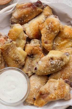 Baked chicken wings in a bowl lined with parchment paper and next to a small dish of ranch dressing.