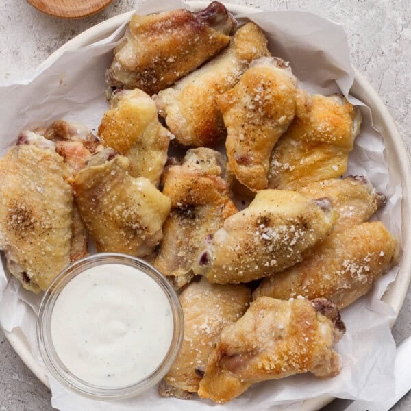 Baked chicken wings in a bowl lined with parchment paper and next to a small dish of ranch dressing.
