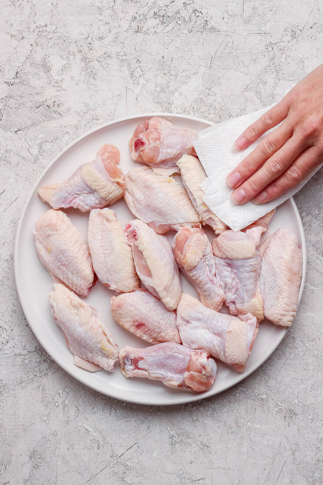 Chicken wings being pat dry with paper towel on a plate before becoming baked chicken wings.