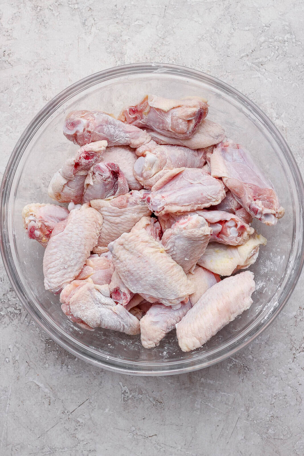 Chicken wings tossed in baking powder in a glass bowl before going in the oven to become baked chicken wings.