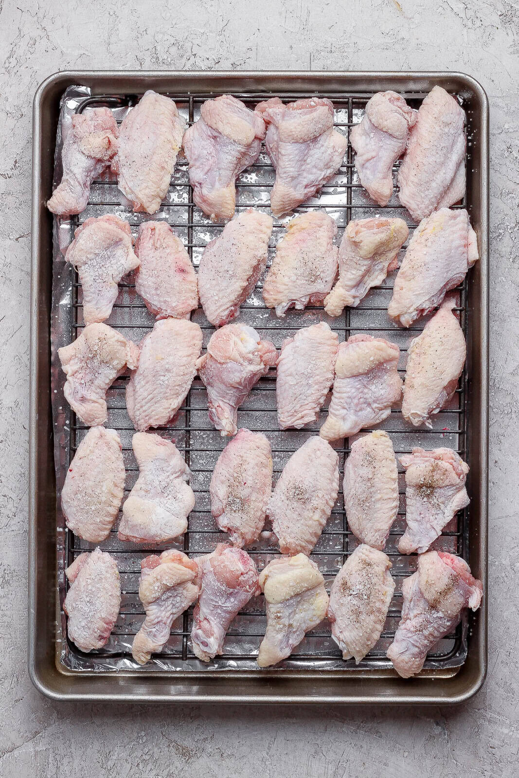 Baked chicken wings on a wire rack on a sheet pan before baking.