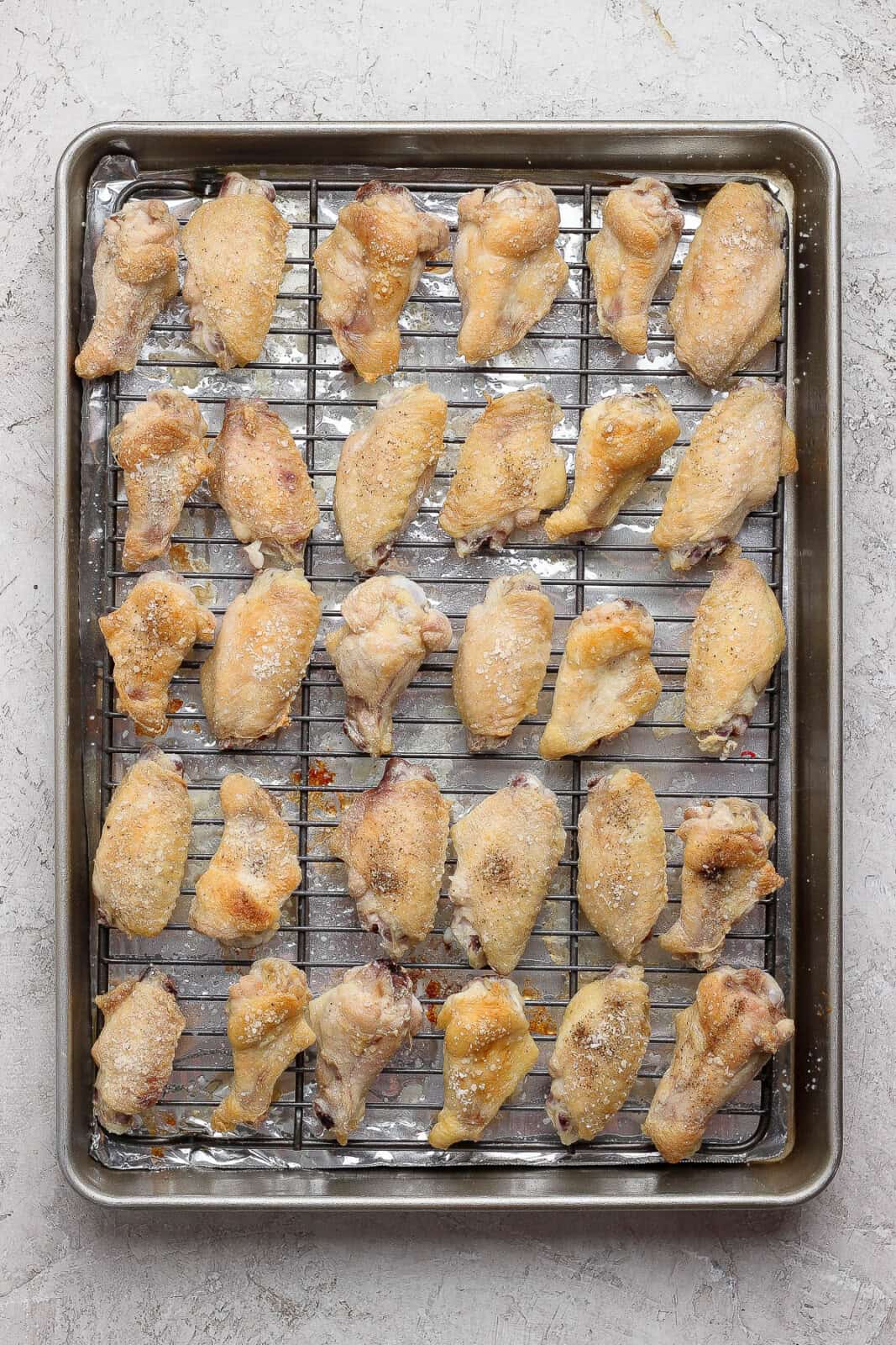 Baked chicken wings on a wire rack on a sheet pan after baking.