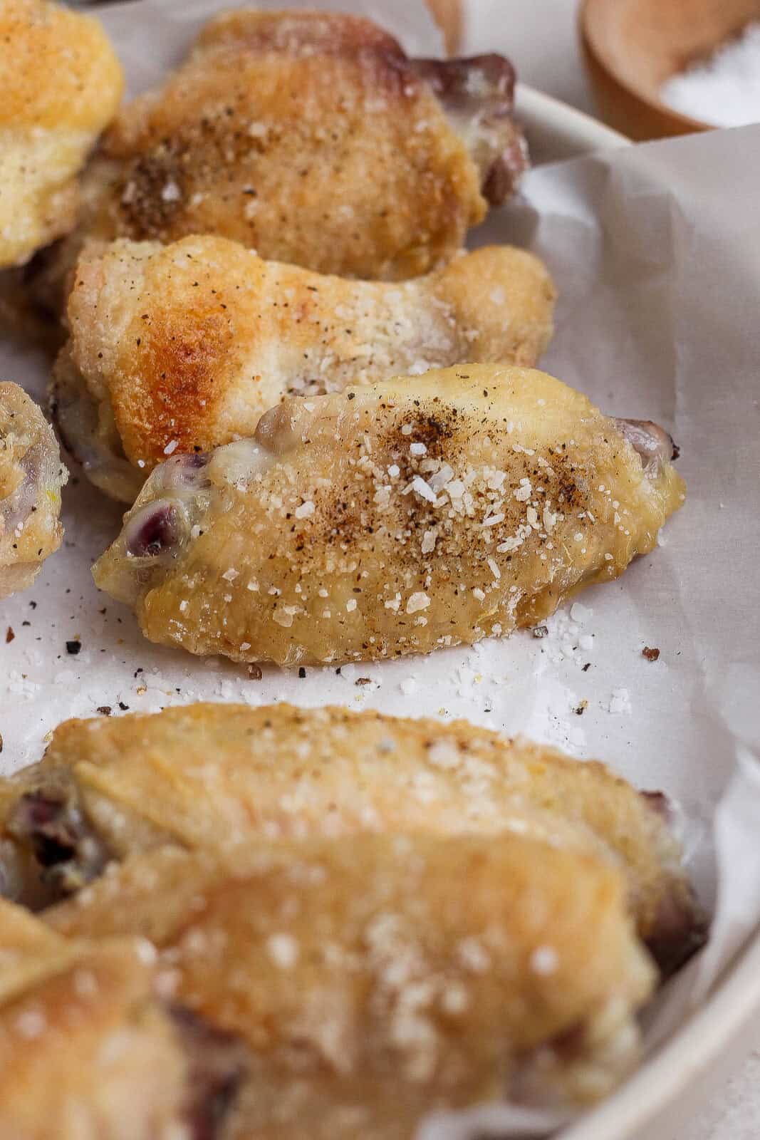 Baked chicken wings on parchment paper with salt and pepper on them.