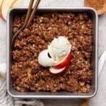 A pan of healthier apple crisp with a scoop of ice cream and sliced apples on top.