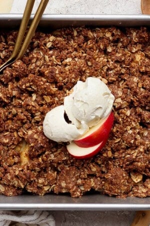 A pan of healthier apple crisp with a scoop of ice cream and sliced apples on top.