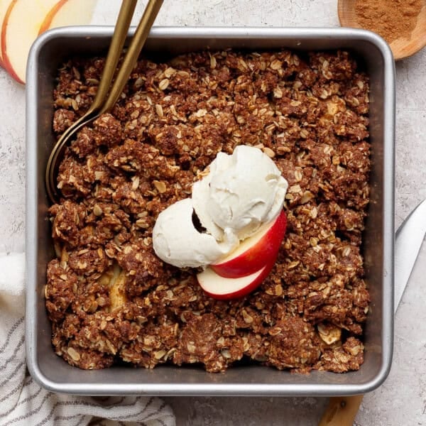 A pan of healthier apple crisp with a scoop of ice cream and sliced apples on top.